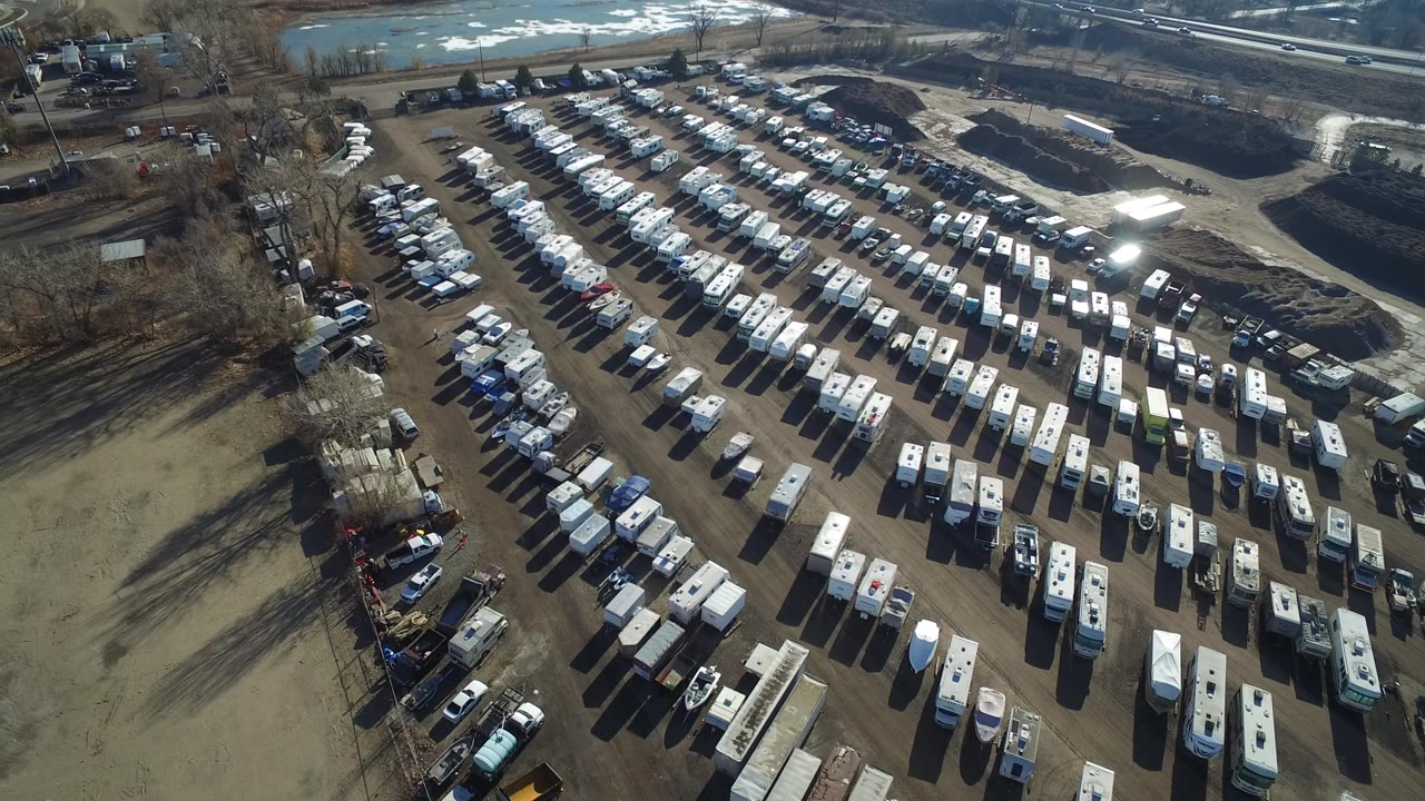 Aerial view of a large dirt parking lot filled with cars, trucks, and trailers.