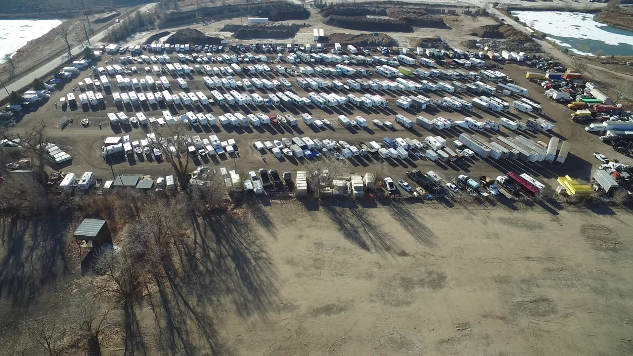 Aerial view of rows of parked vehicles beside open fields and bare trees.