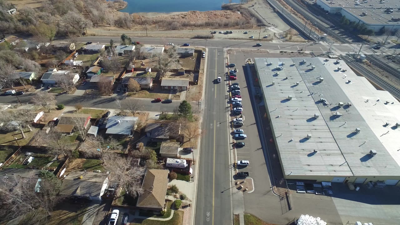 Aerial view of a flat-roofed building beside houses and roads near water.