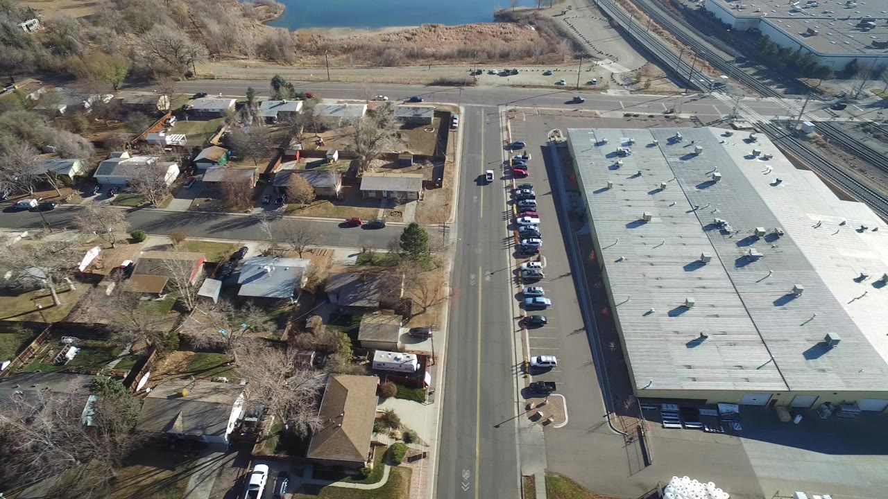 A second aerial frame in Hidden Lake, Colorado holds on the long roof and surrounding houses while the road grid, parked vehicles, bare trees, and waterline remain visible, with no visible people identifiable.