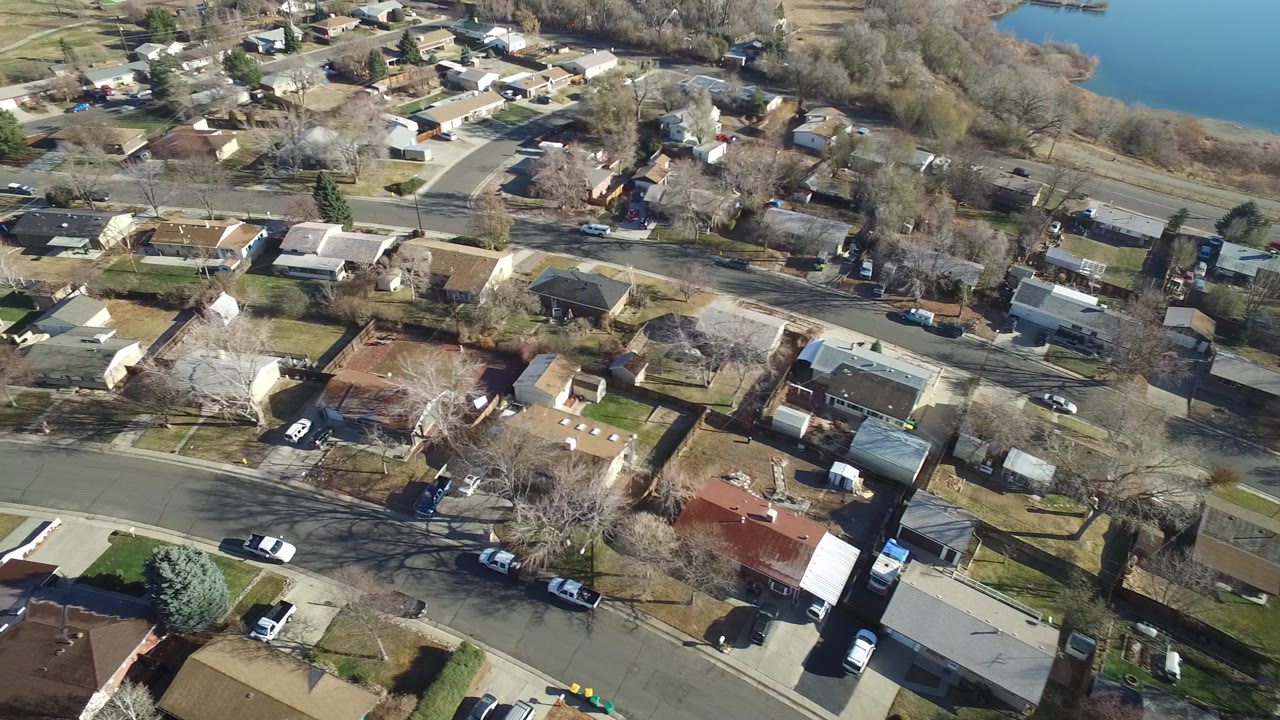 Residential rooftops and streets near a wooded lake shoreline.