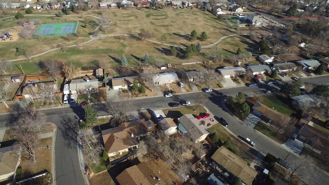 Aerial view over Hidden Lake, Colorado homes beside a park with green tennis courts, a small playground, curving paths, leafless trees, and no recognizable people.