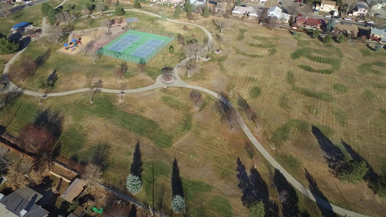 Overhead park view with tennis court, paths, lawns, trees, and houses