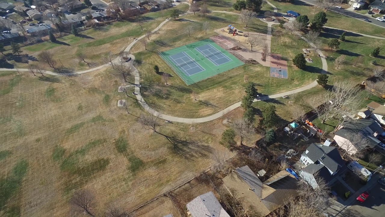 Aerial park view with tennis courts, playground, lawns, and houses.