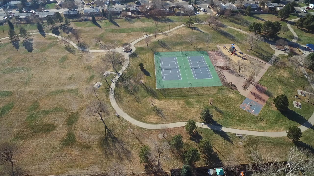Aerial frame over Hidden Lake, Colorado showing tennis courts near the center, a small basketball court below, curving paths, winter-bare trees, and houses along the top edge.
