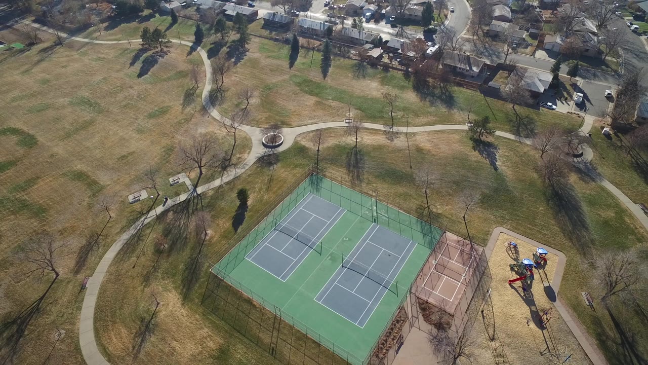 Aerial view of fenced tennis courts beside paths and homes.