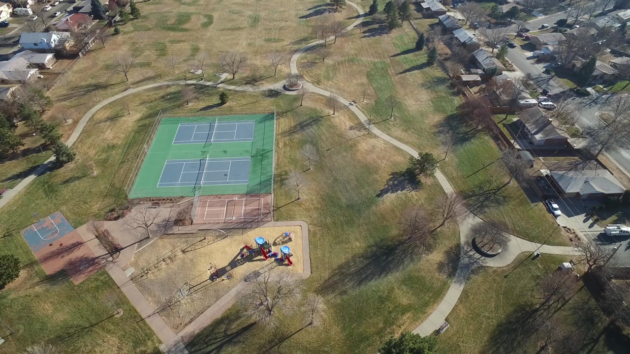 Aerial park frame with tennis courts, playground, curved paths, and houses.