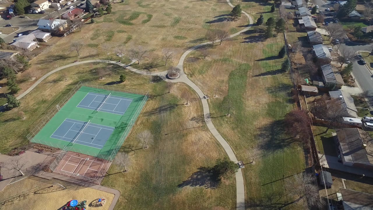 Aerial view of tennis courts, grass field, paths, and nearby houses.