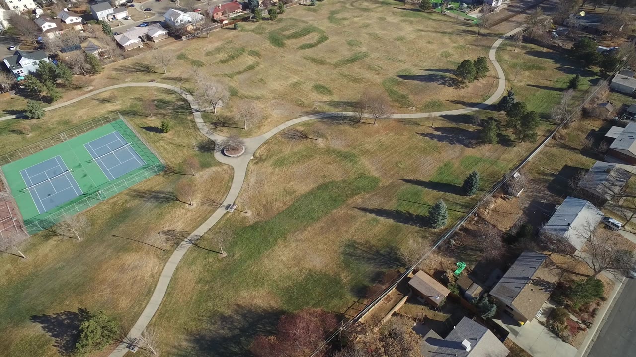 Aerial view of open grass, tennis courts, paths, trees, and nearby houses.