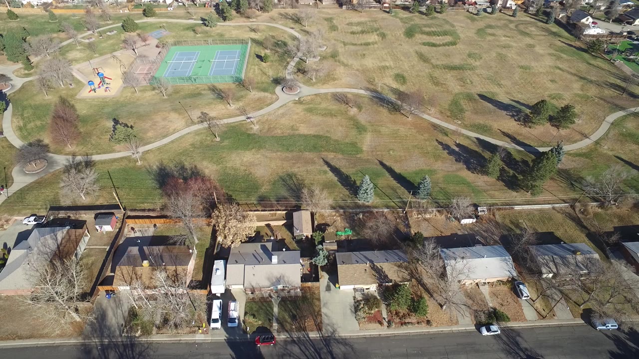 Aerial view of homes, a road, open grass, tennis courts, and park paths.