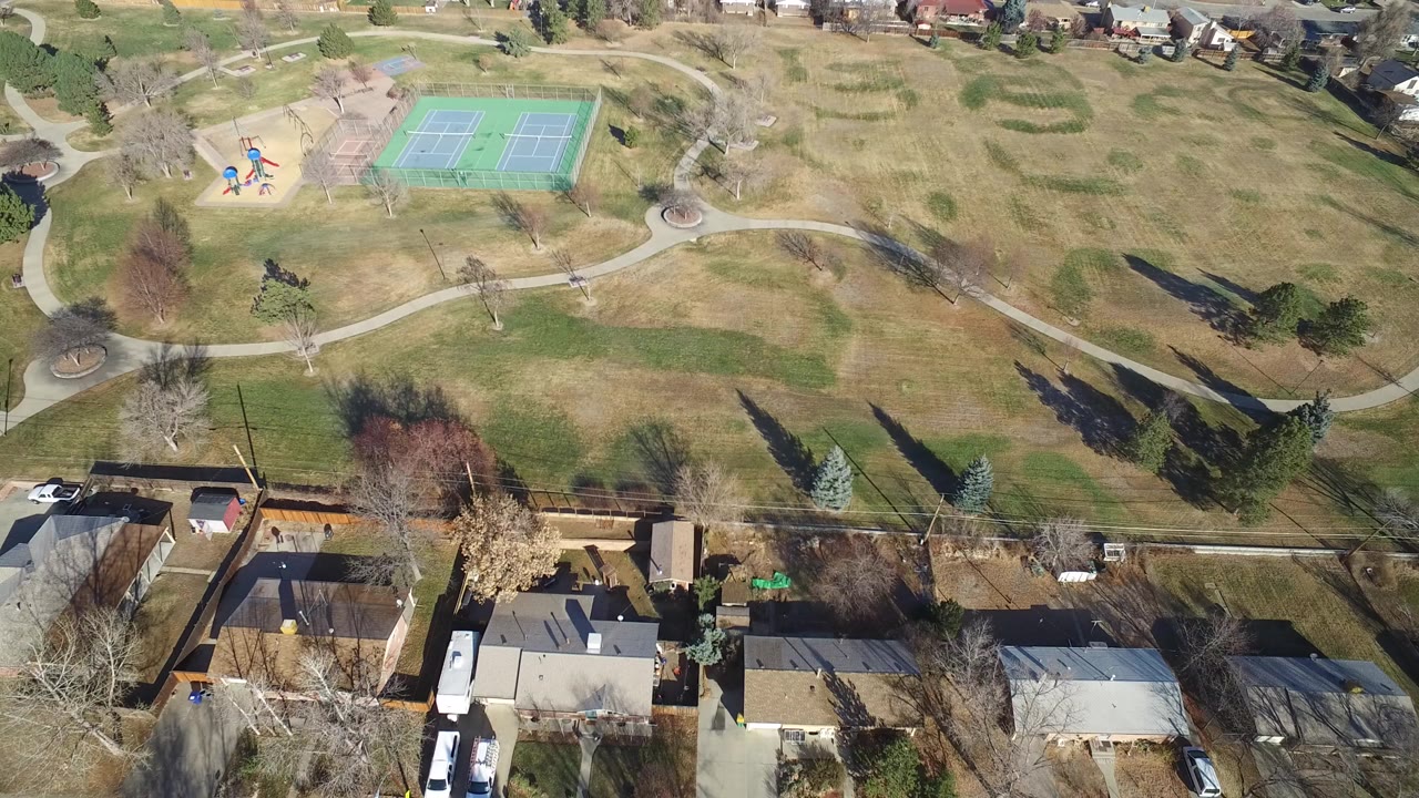 Aerial view of a park with tennis courts, playground, paths, and nearby homes.