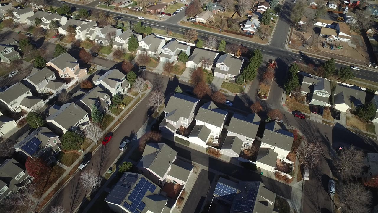 High aerial view over Hidden Lake, Colorado homes, fenced yards, leafless trees, and a broad road intersection at the start of the clip, with no visible people.