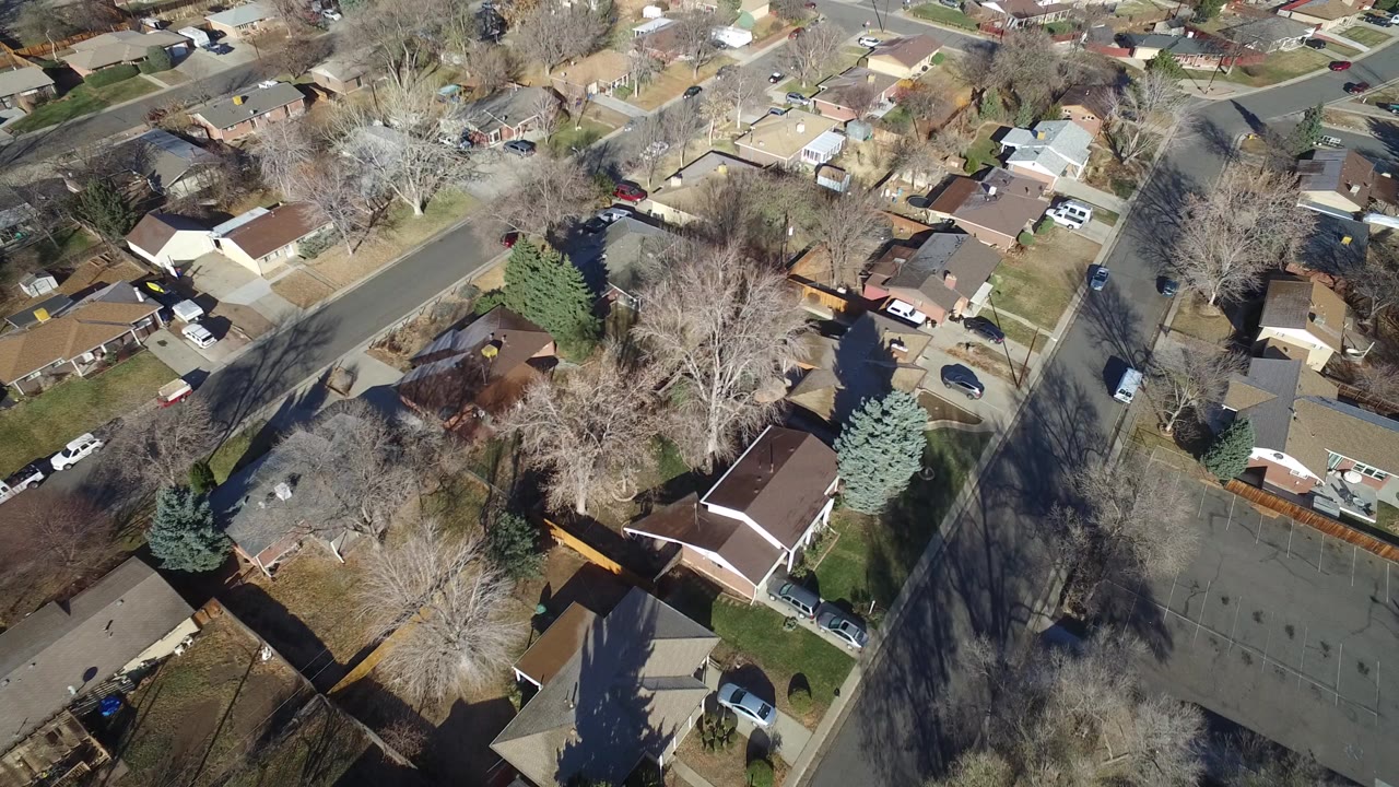 High-angle aerial view over Hidden Lake, Colorado homes, bare trees, fenced yards, parked cars, and intersecting residential streets, with no clearly identifiable people visible.