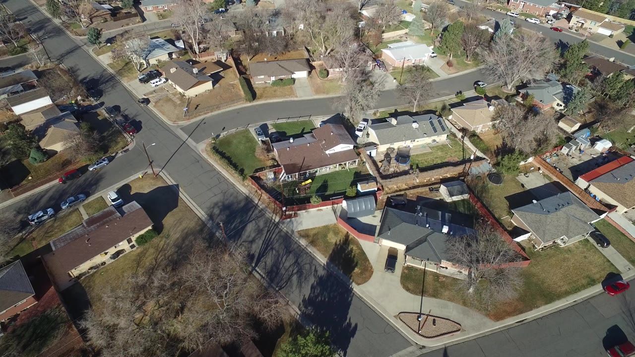 High aerial view over Hidden Lake, Colorado homes at a street corner, with fenced yards, driveways, leafless trees, long shadows, and no visible people.