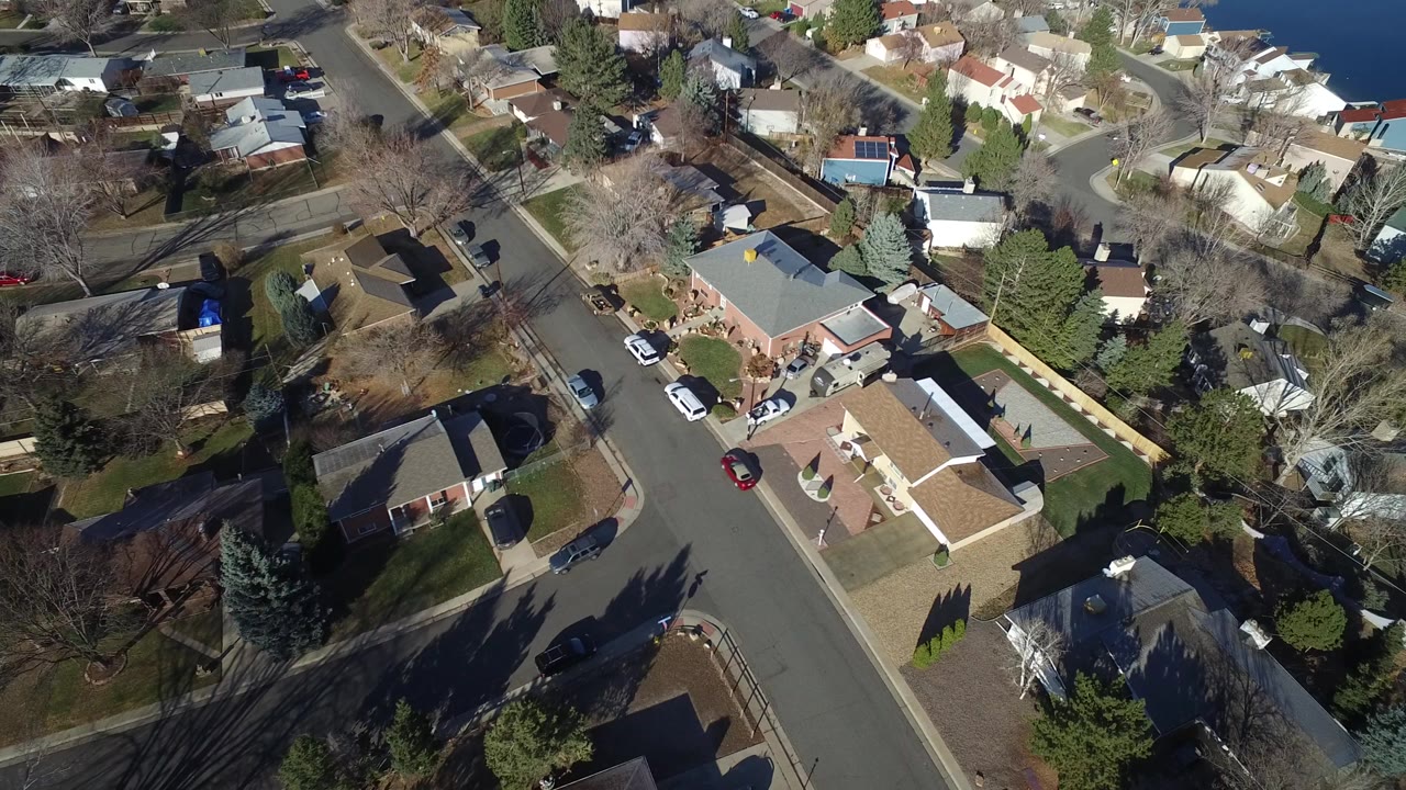 Aerial view of residential streets, houses, cars, trees, and lake water