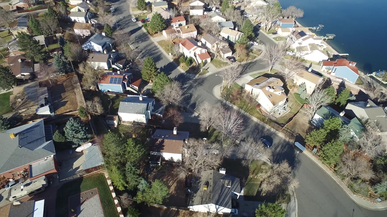 Overhead view of Hidden Lake, Colorado residential streets and houses, with bare trees casting shadows and dark blue lake water on the right, with no visible people.