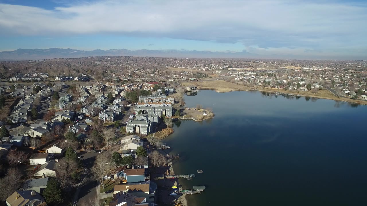 Aerial view of a blue lake beside residential buildings and distant mountains.