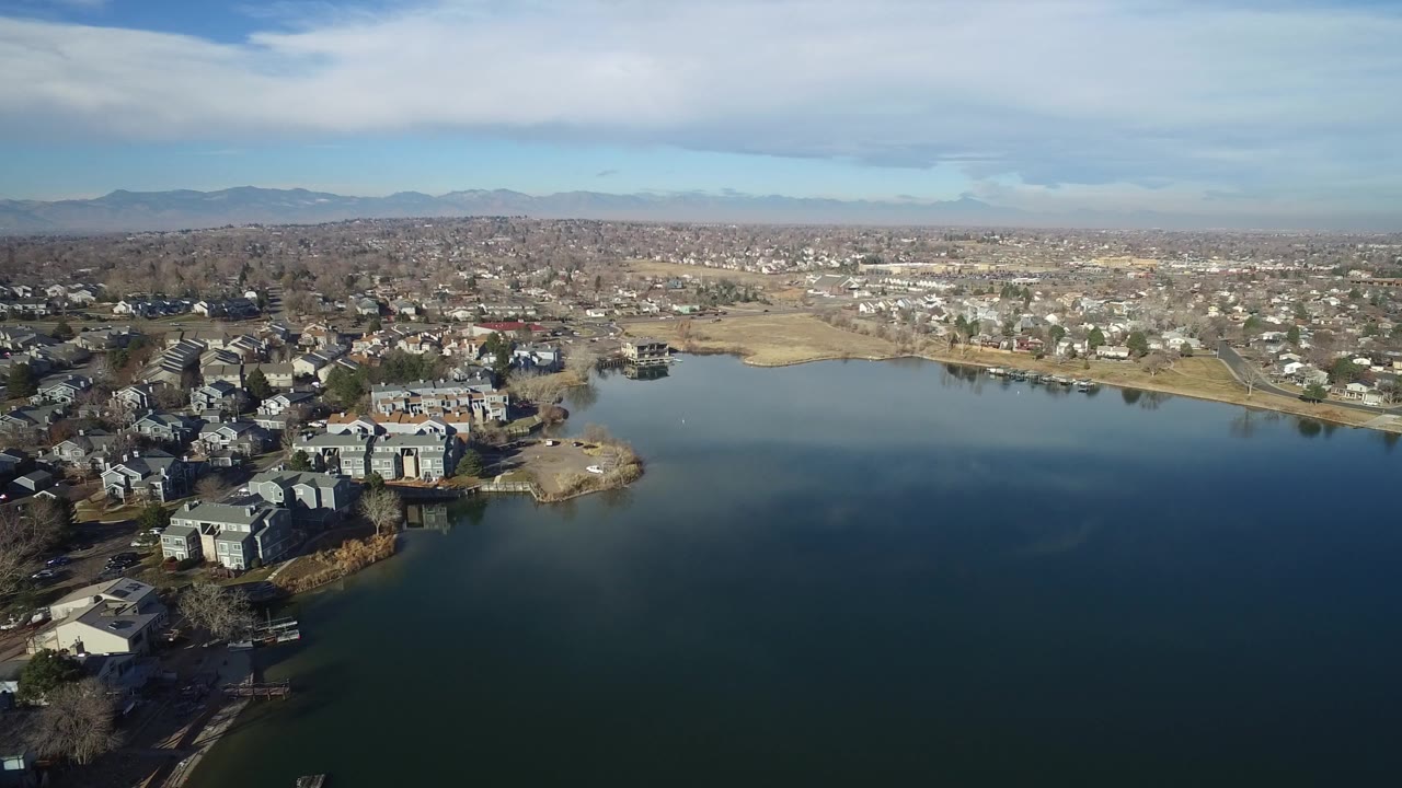 Aerial view over a lake with shoreline homes and distant hills.