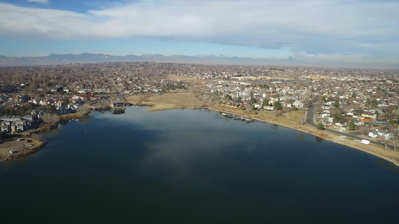 Aerial view of Hidden Lake, Colorado with the lake across the lower frame, shoreline houses and roads in the middle distance, mountains on the horizon, and no visible people.