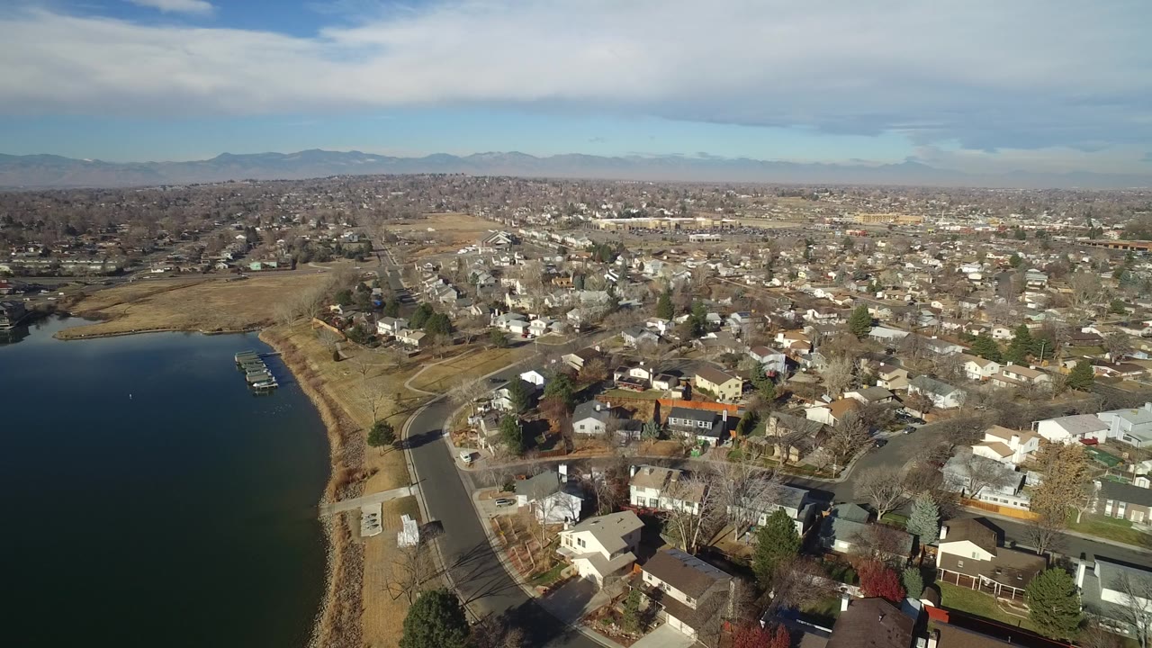 Aerial view of a lake edge, docks, roads, houses, trees, and distant mountains.