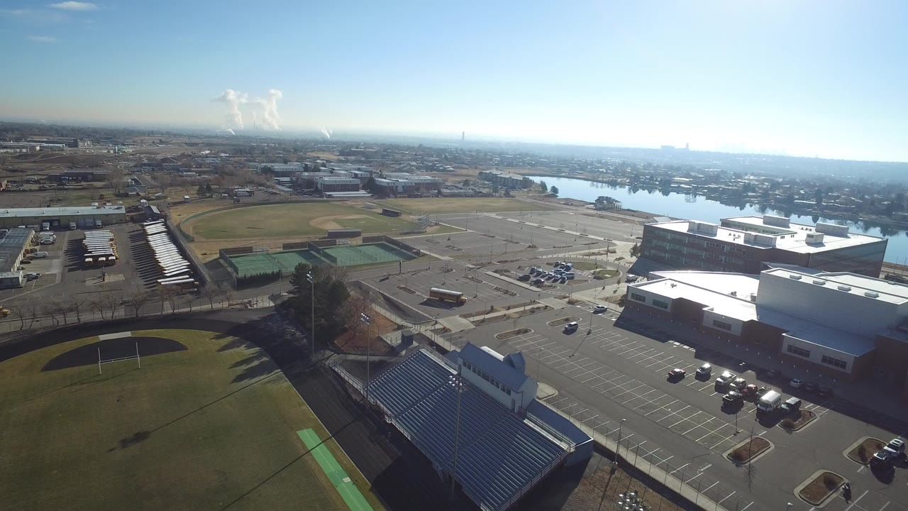 Aerial view of sports fields, parking lots, buildings, roads, and a river beyond.