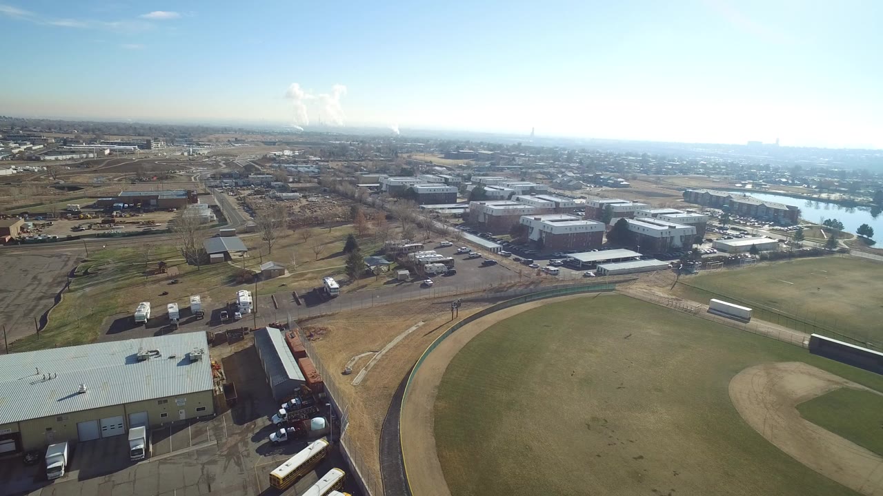 Aerial view of industrial buildings, fields, roads, and distant water under a blue sky.