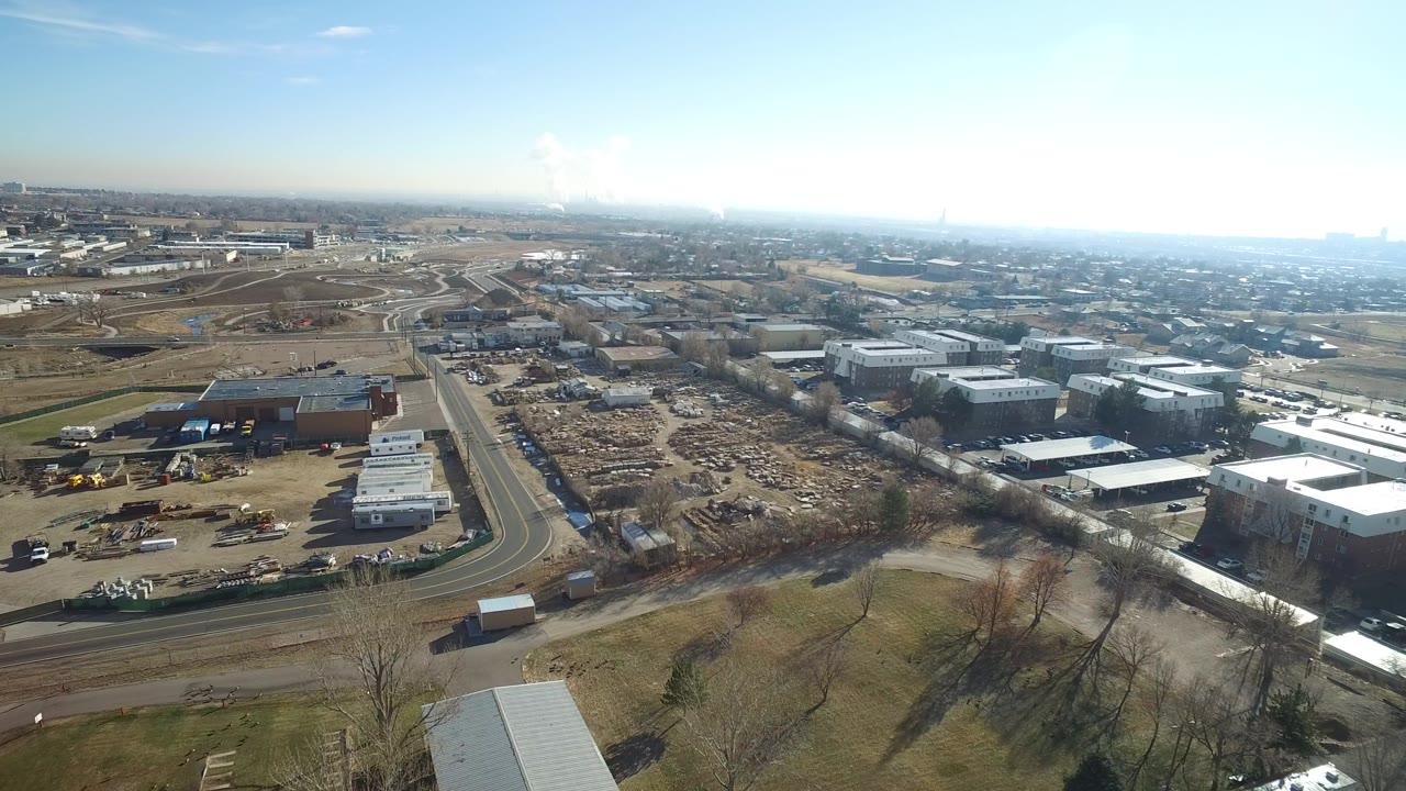 Aerial view of curving roads, industrial lots, and distant neighborhoods under a blue sky.
