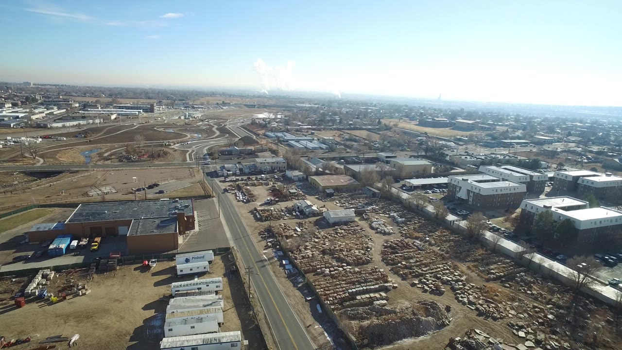 Drone view in Hidden Lake, Colorado looking across dense rows of scrapped cars, industrial lots, flat-roof buildings, roadway lanes, and no visible people.