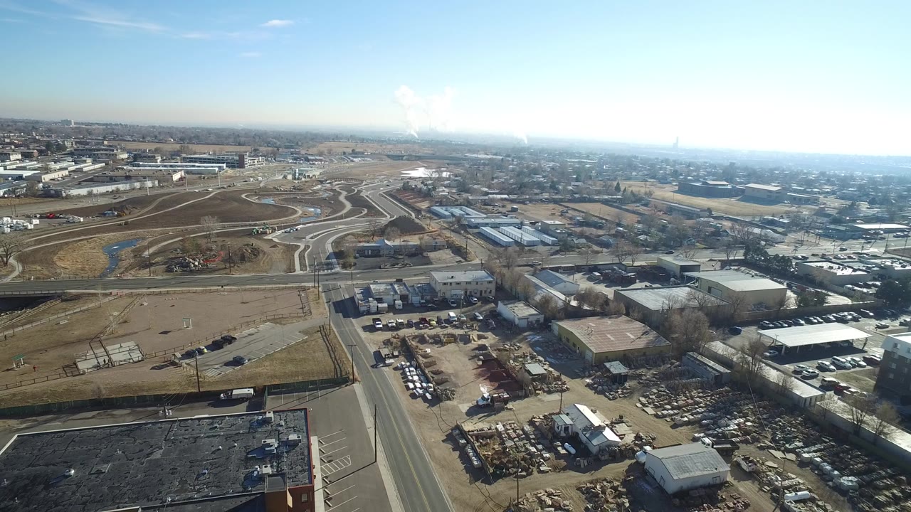 Aerial view over roads, industrial lots, and low buildings under a bright sky.