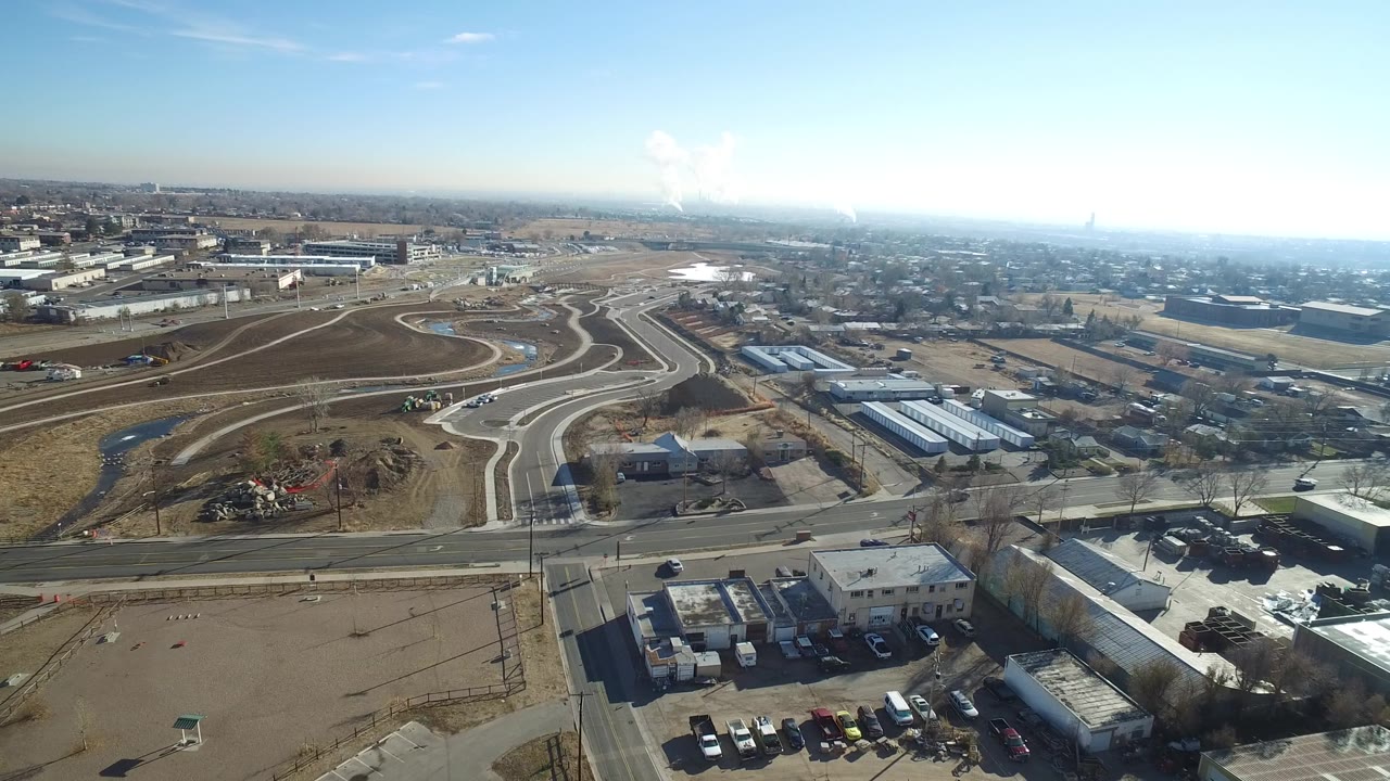 Opening aerial frame over Hidden Lake, Colorado, with curving pale roads crossing brown open land, low buildings and homes below, distant smoke on the horizon, and no visible people.