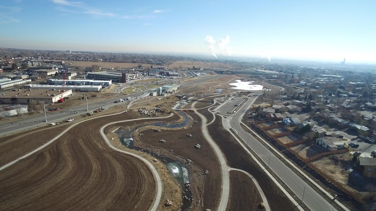 Aerial frame over Hidden Lake, Colorado with brown graded land in the foreground, looping roads through the center, buildings and houses beyond, pale sky above, and no visible people.