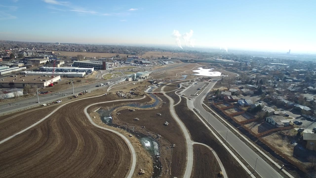 Aerial view in Hidden Lake, Colorado with a curved roadway crossing open soil, a small drainage channel, low buildings at left, houses at right, and no visible people.