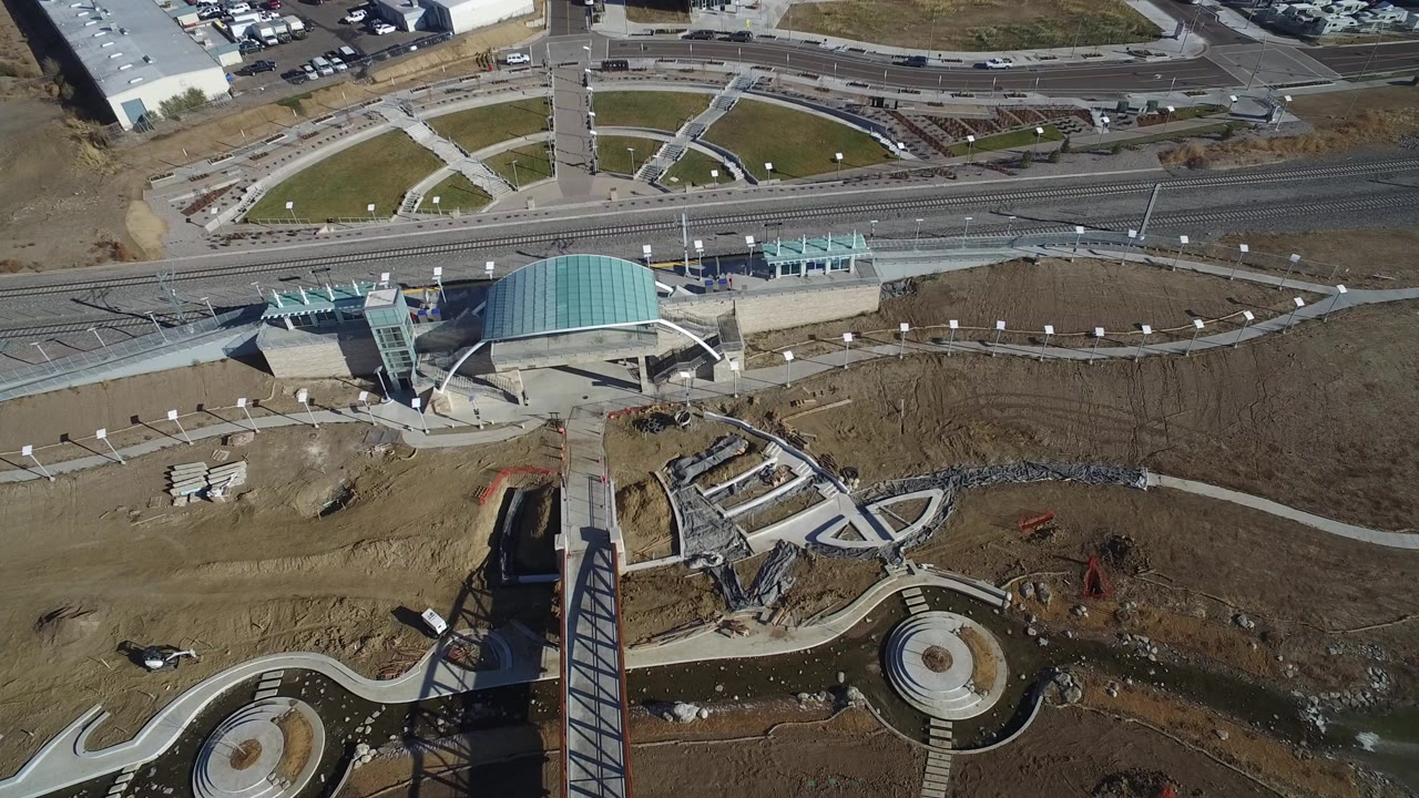 Aerial view of a designed park with paths, bridge, roads, and a turquoise-roofed structure.