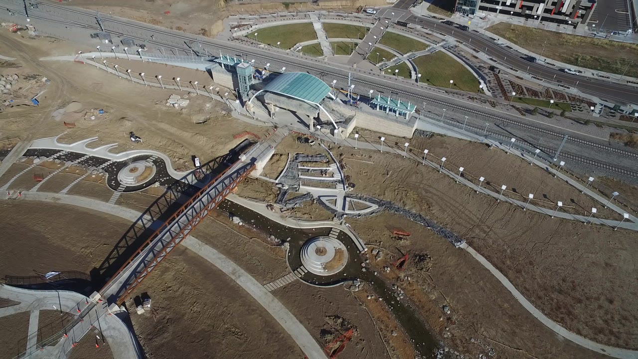 Aerial view of pedestrian bridge, circular plazas, paths, roads, and rail tracks.