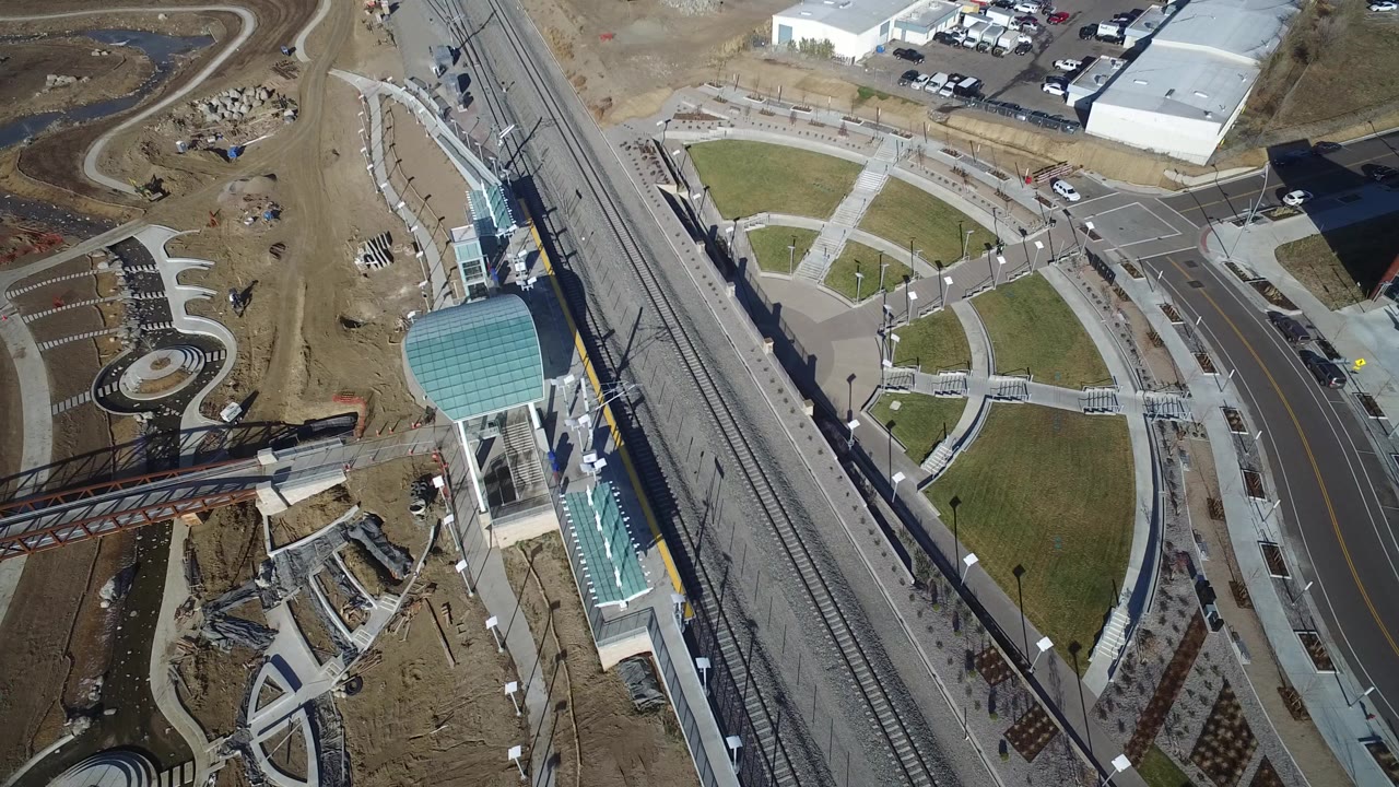 Overhead view of rail tracks, a road, landscaped paths, and a teal-roofed pedestrian structure.