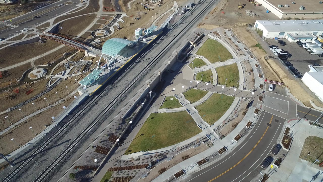 Aerial view of rail tracks crossing beside a small station and curved sidewalks.