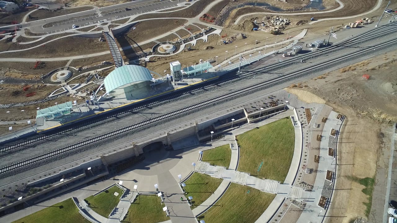 Drone view of rail tracks, a pale dome, road curves, lawns, and dirt lots.