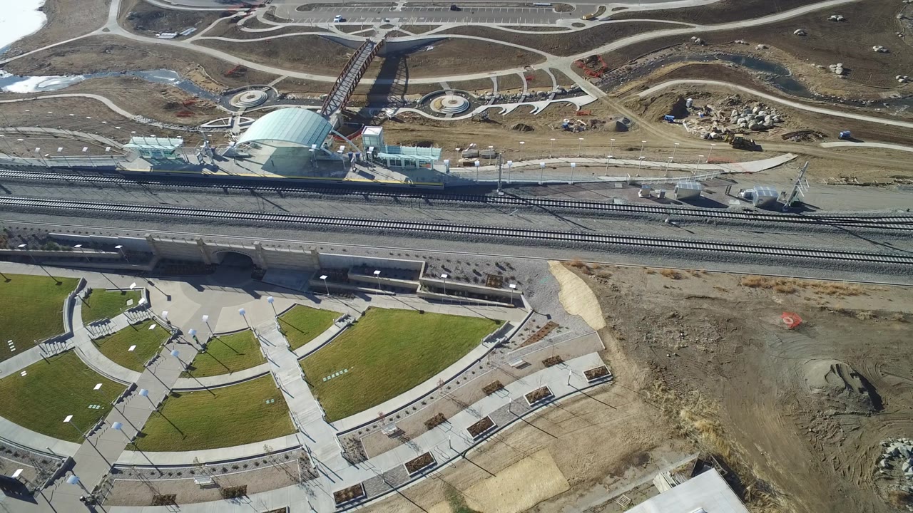 Aerial view in Hidden Lake, Colorado with the curved lawn shifted slightly across frame, rail lines crossing the middle, a road corridor above, and no recognizable people.