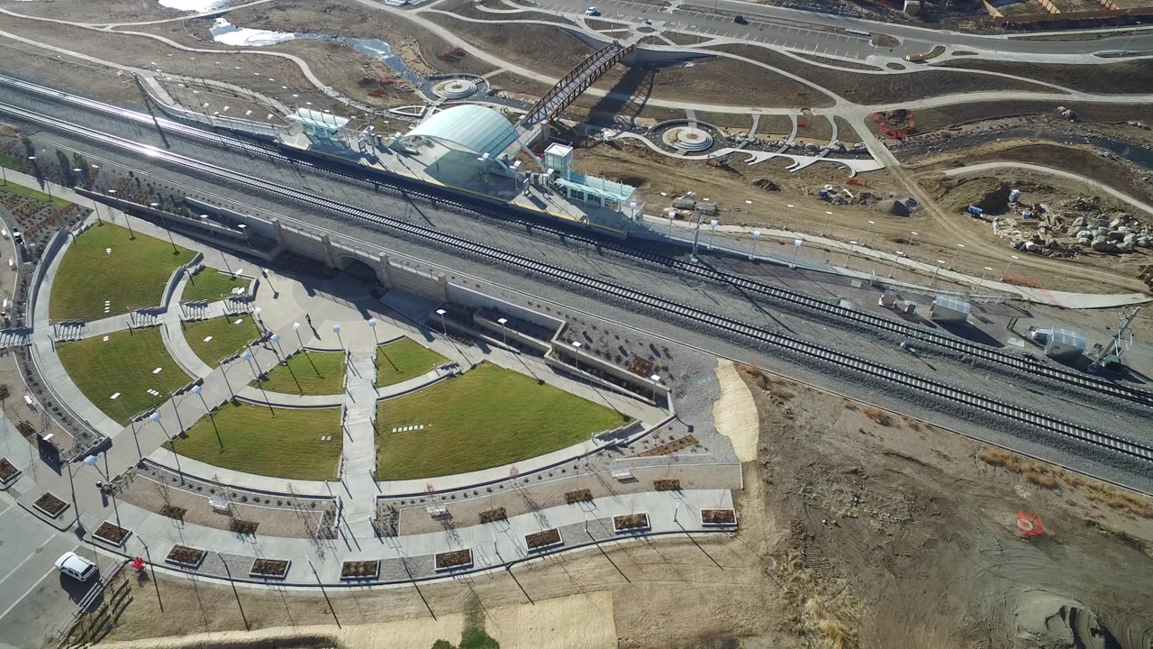 Hidden Lake, Colorado aerial frame showing highway lanes, rail tracks, a landscaped plaza with curved walkways, a small vehicle, and no visible people.