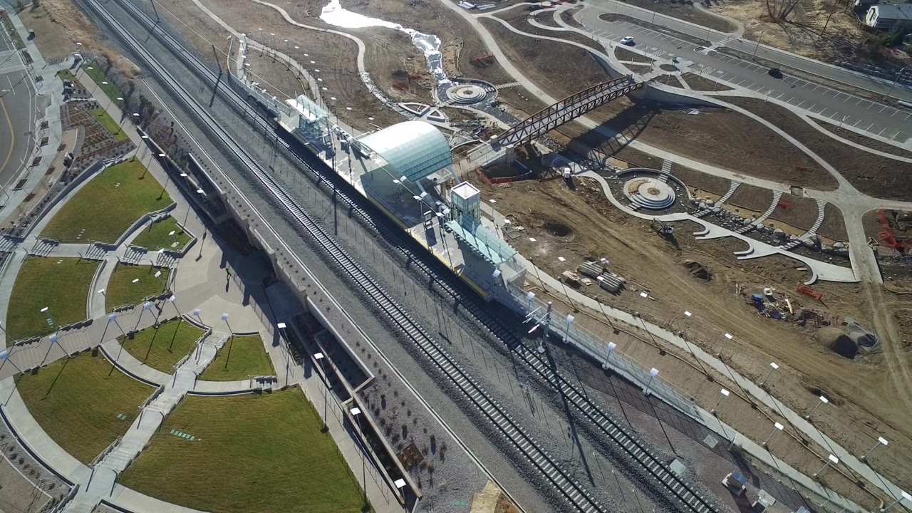 Aerial view of railroad tracks beside a station and landscaped paths.