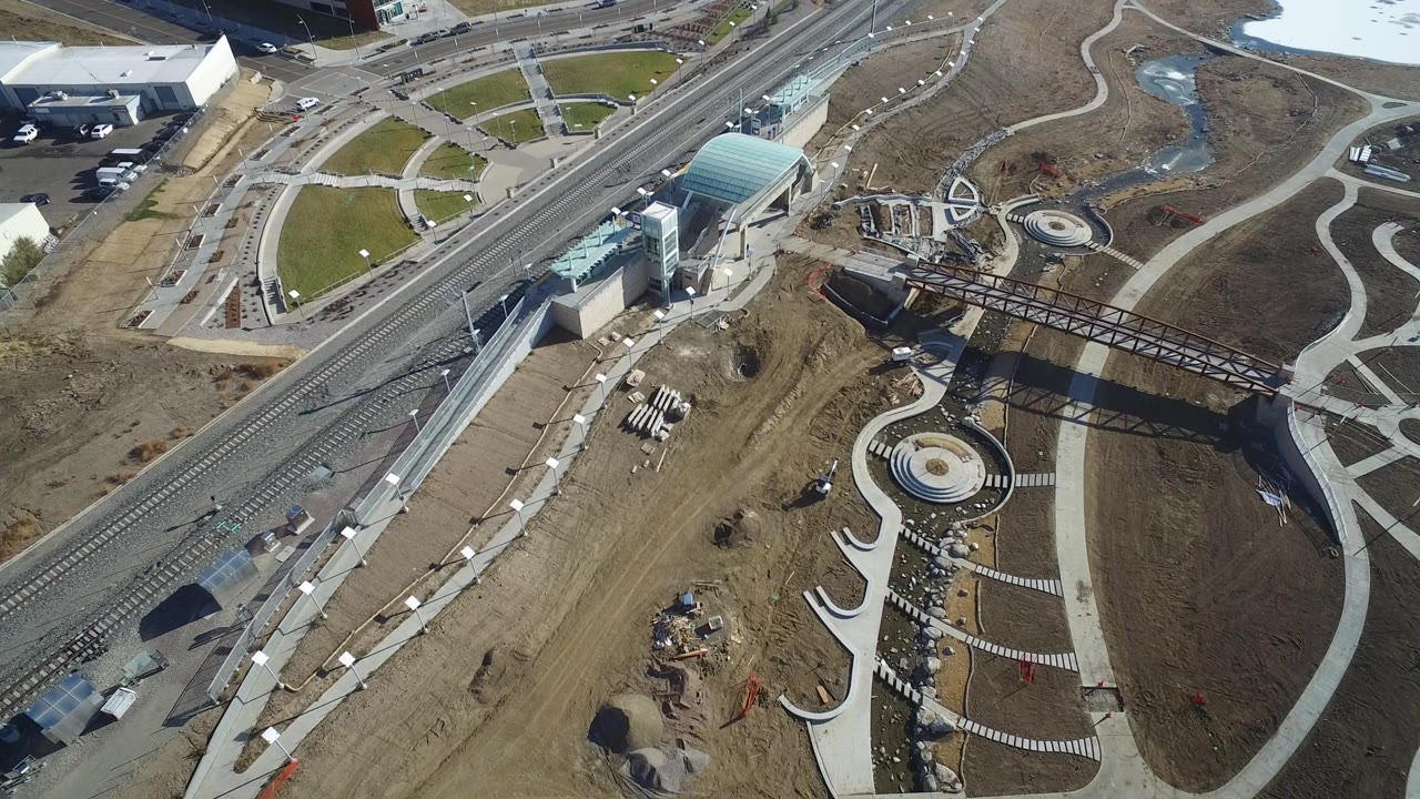 High aerial frame over Hidden Lake, Colorado showing rail tracks, a glass-roofed structure, circular plaza features, curving paths, brown ground, and no visible people.
