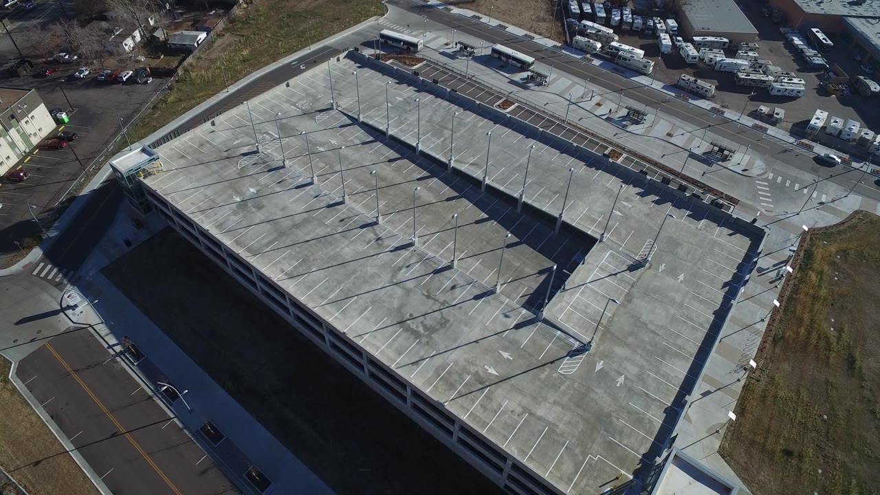 A slightly shifted aerial view in Hidden Lake, Colorado keeps the concrete roof deck centered, with white parking lines, pole shadows, surrounding pavement, and no visible people.