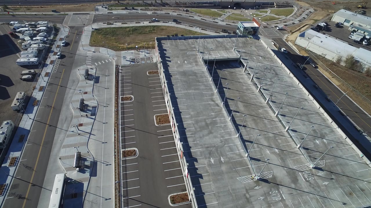Aerial view of a large warehouse roof and empty parking lot beside roads.