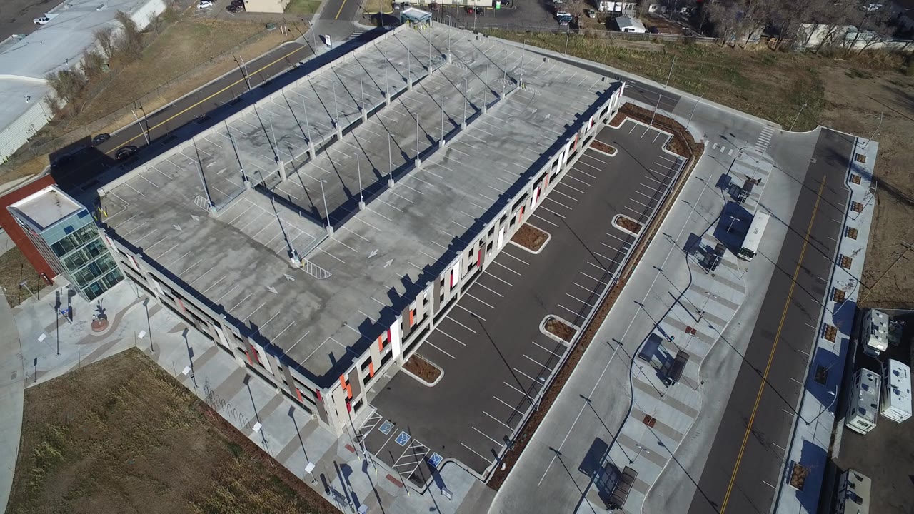 Opening aerial frame over Hidden Lake, Colorado, showing a flat-roofed commercial-looking building, rooftop parking layout, empty side lot, surrounding roads, winter-brown grass, and no visible people.