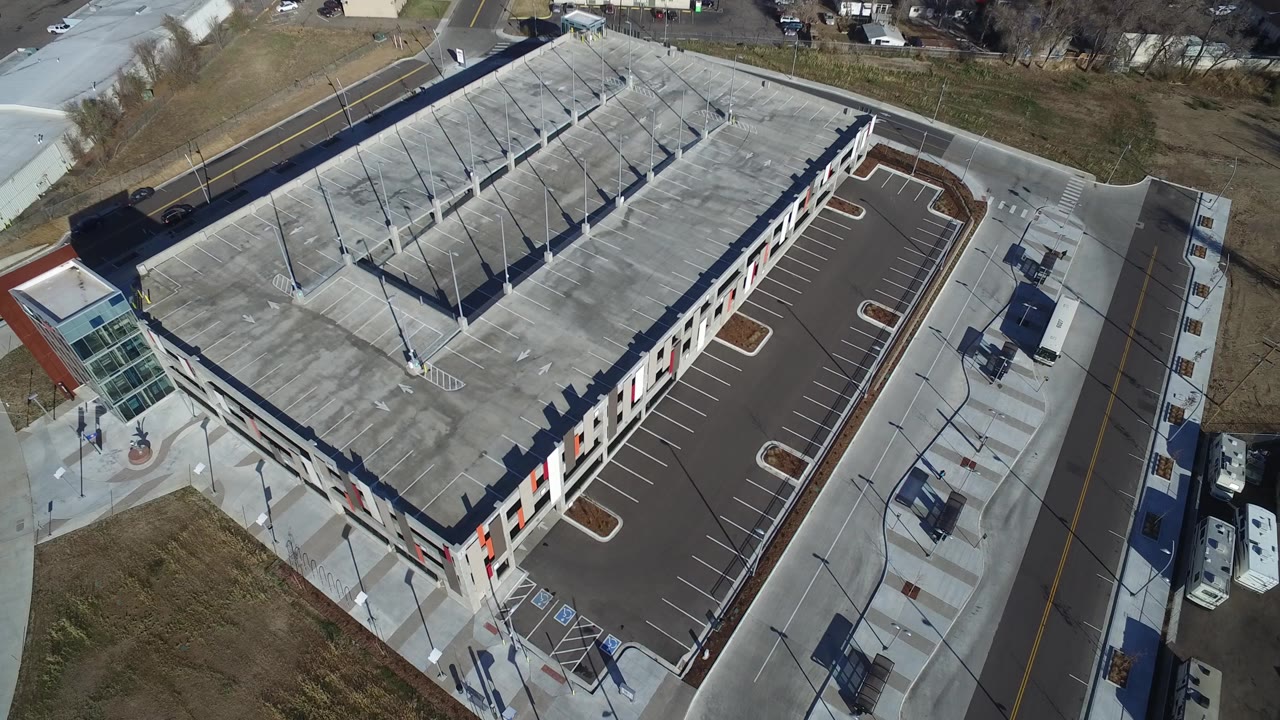 Aerial frame in Hidden Lake, Colorado, with the roof plane filling the center, striped parking stalls and light poles casting long shadows, access roads on two sides, and no visible people.