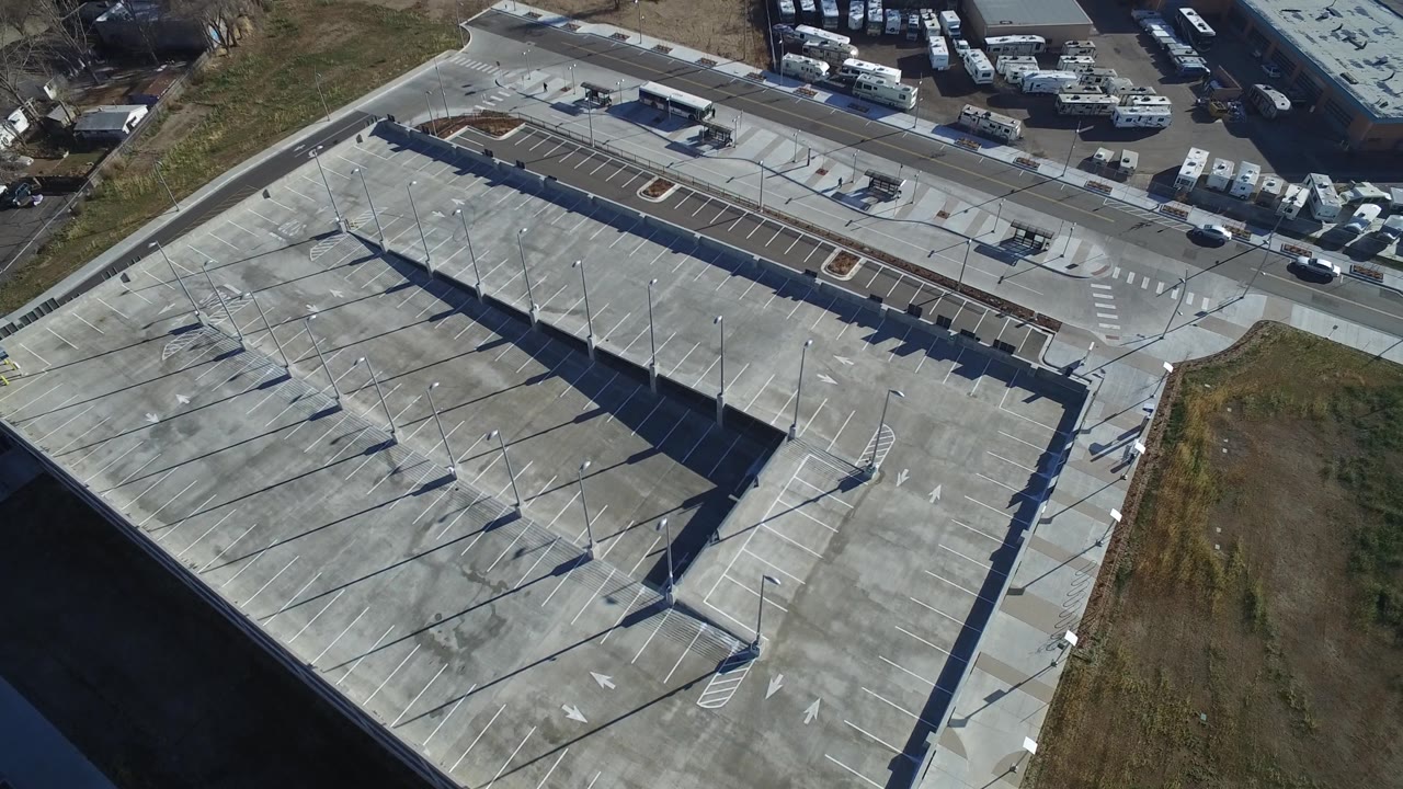 High drone view of parking garage ramps, roadway, grass, and parked trailers.