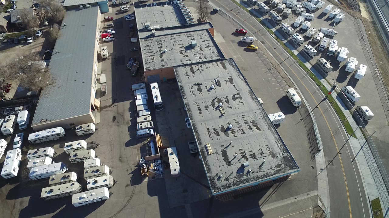 Overhead view of flat-roof buildings, parked RVs, cars, and a curved road.