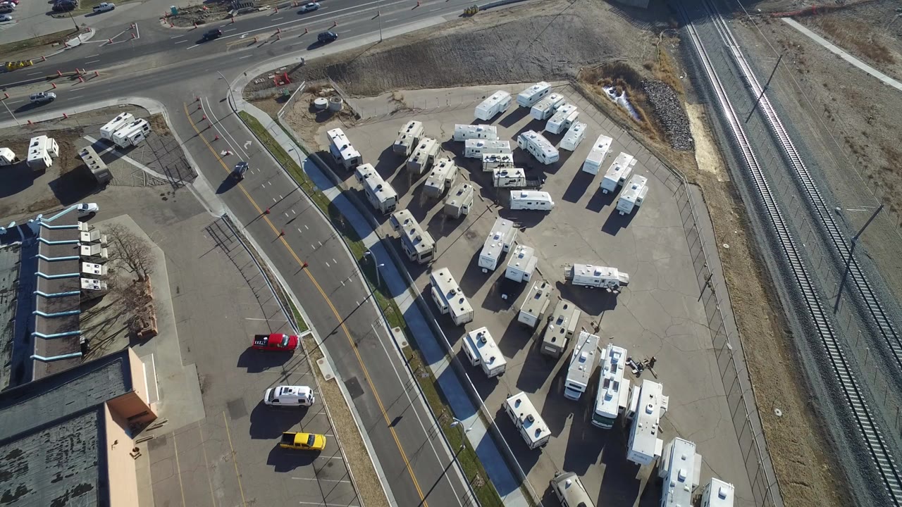 Aerial frame from Hidden Lake, Colorado showing white RVs and trailers parked near an intersection, rail tracks on the right, and no visible people.