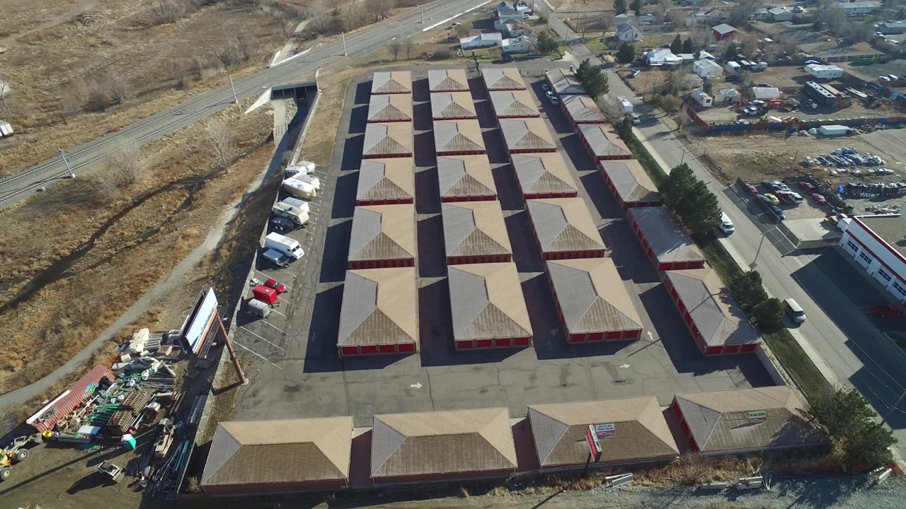 Drone view over red industrial buildings, parking areas, a road, and a storage yard.
