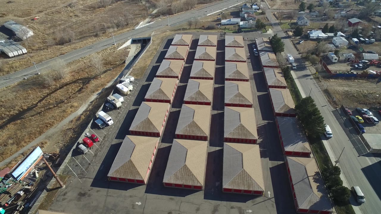 Overhead view of red-sided buildings with tan roofs near houses and parked vehicles.